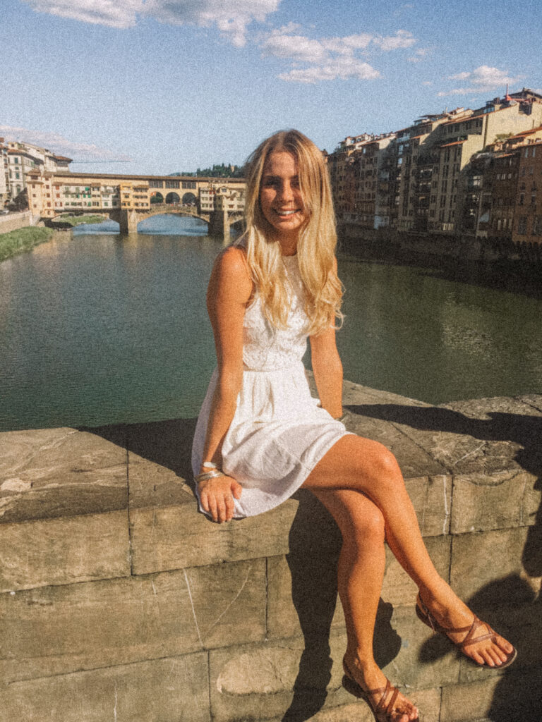 how italians will know you are american - blonde girl in white dress posing for a photo in front of the ponte vecchio in florence