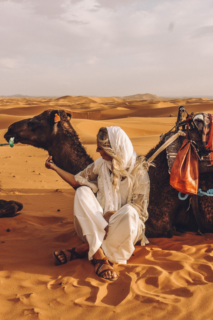 Girl sitting in the desert with a camel in Morocco. 