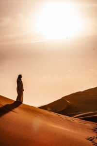 A girl in the dunes of the dessert with the sun in the background.