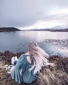 A woman sitting on the coast overlooking the water in the Isle of Skye, Scotland