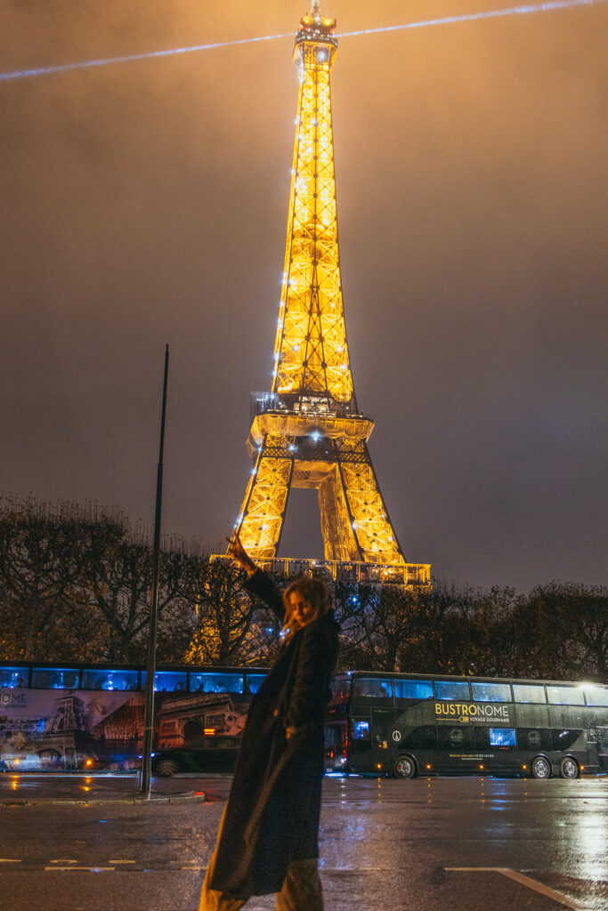 Girl standing outside the Eiffel Tower at night in Paris, France